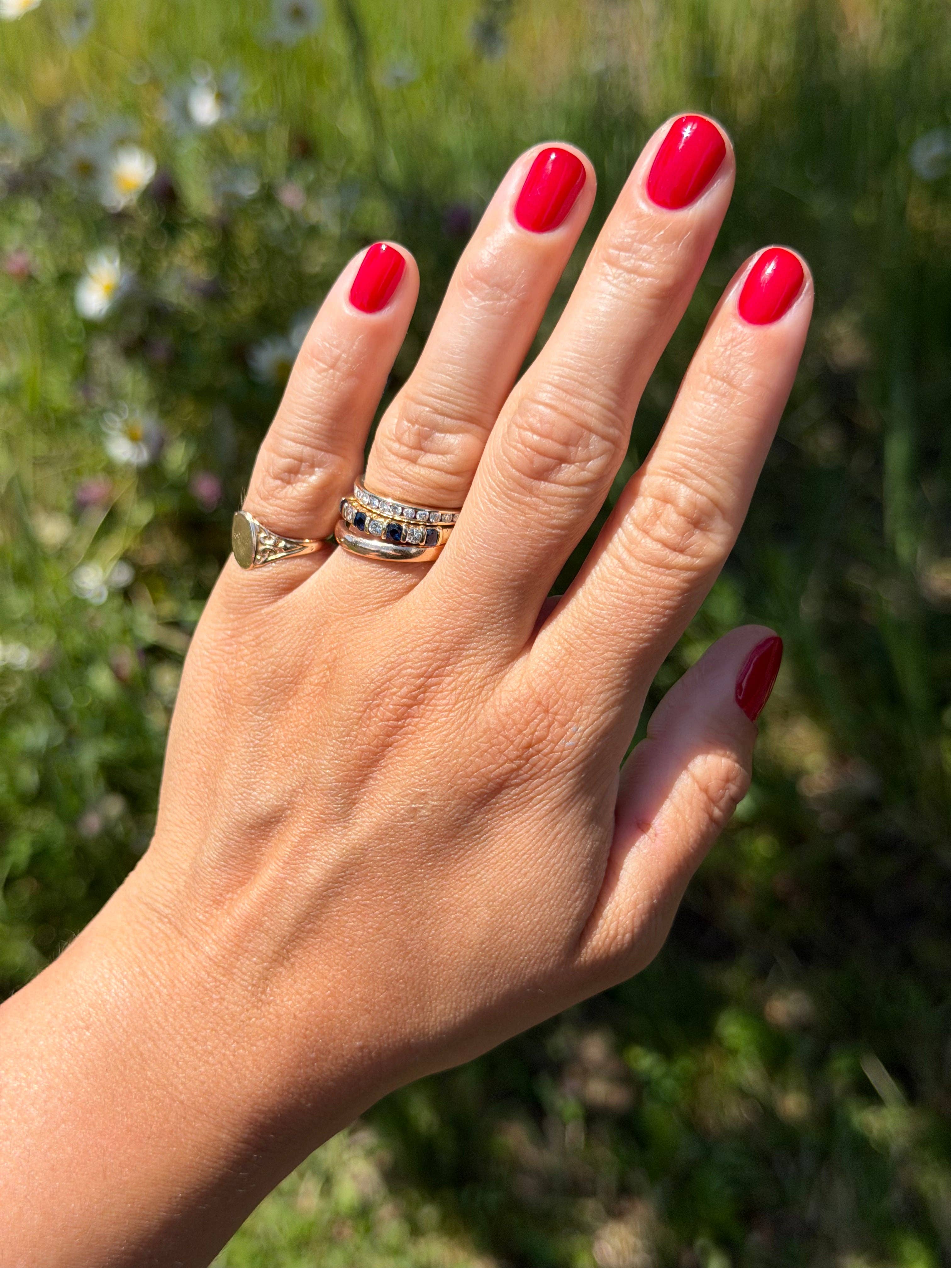 Hand with red nail polish wearing two rings against a blurred green background