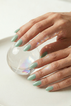 Hand with light green nail polish holding a clear glass ball on a white background