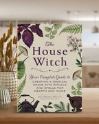 Book titled 'The House Witch' on a wooden surface with decorative elements.