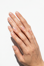 Close-up of a hand with clear nail polish on a light background