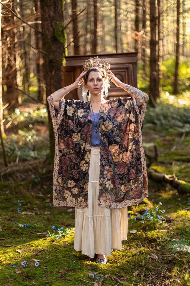 Woman in a floral robe and crown standing in a forest
