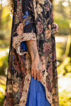 Person wearing a floral patterned garment with a blue skirt in a natural setting