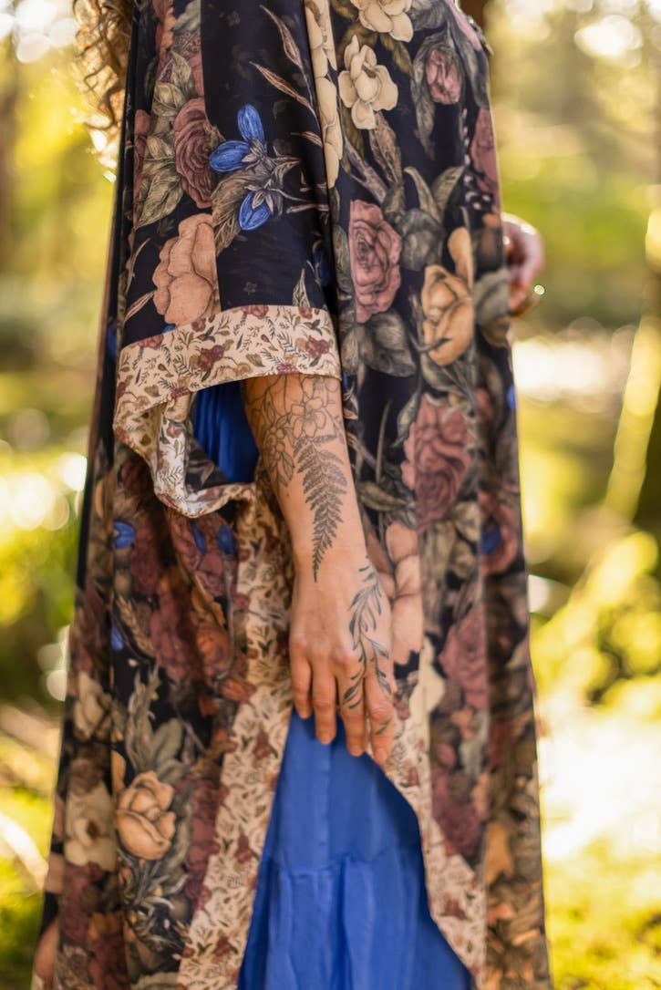 Person wearing a floral patterned garment with a blue skirt in a natural setting