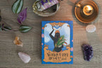 Tarot card deck titled 'The Wandering Heart Deck' by Kevyn Ridgy on a wooden surface with crystals and a candle.