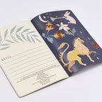 Open notebook with one page featuring a lion illustration and the other with floral design on a white background.