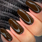 Hand with dark brown nail polish on a textured gray background