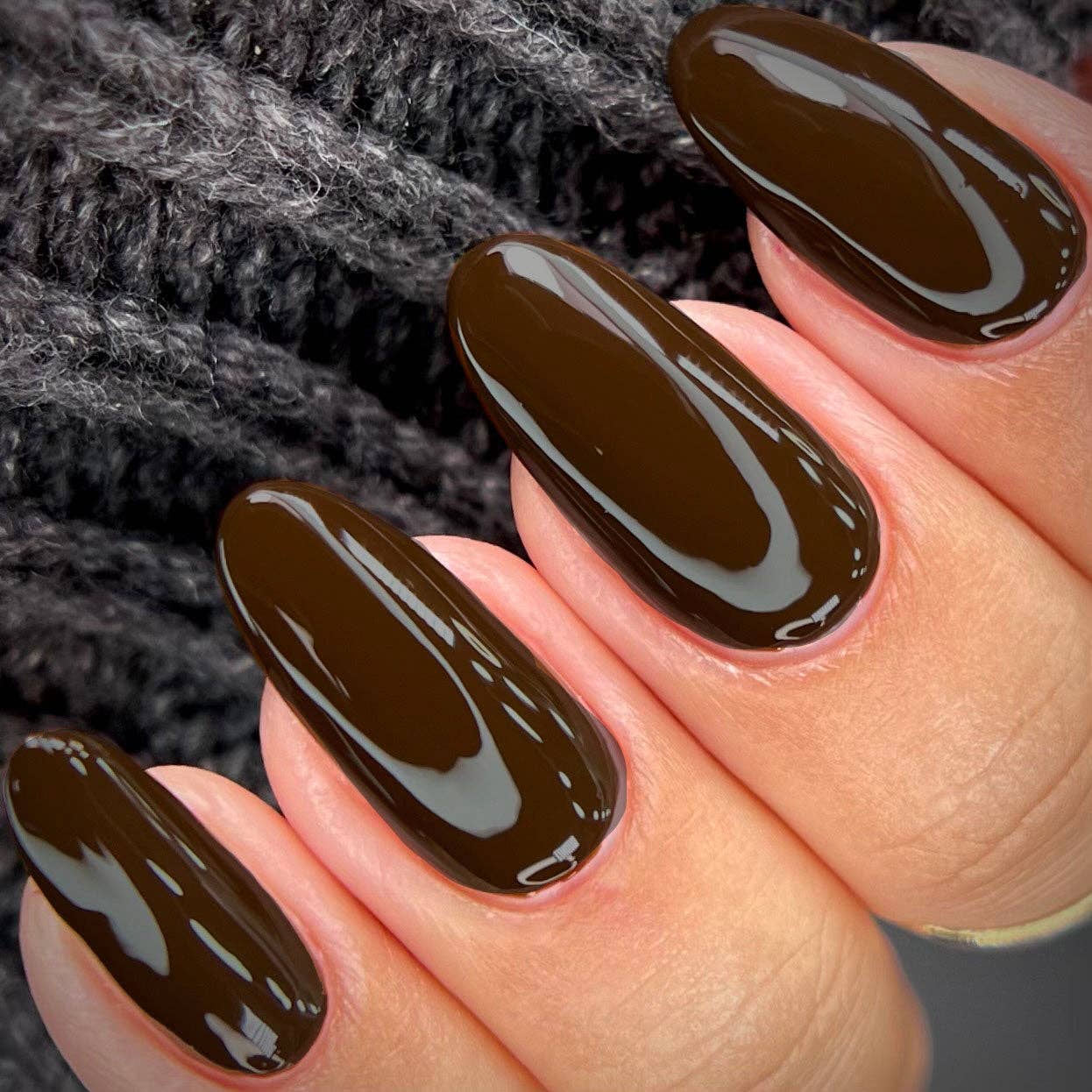 Hand with dark brown nail polish on a textured gray background