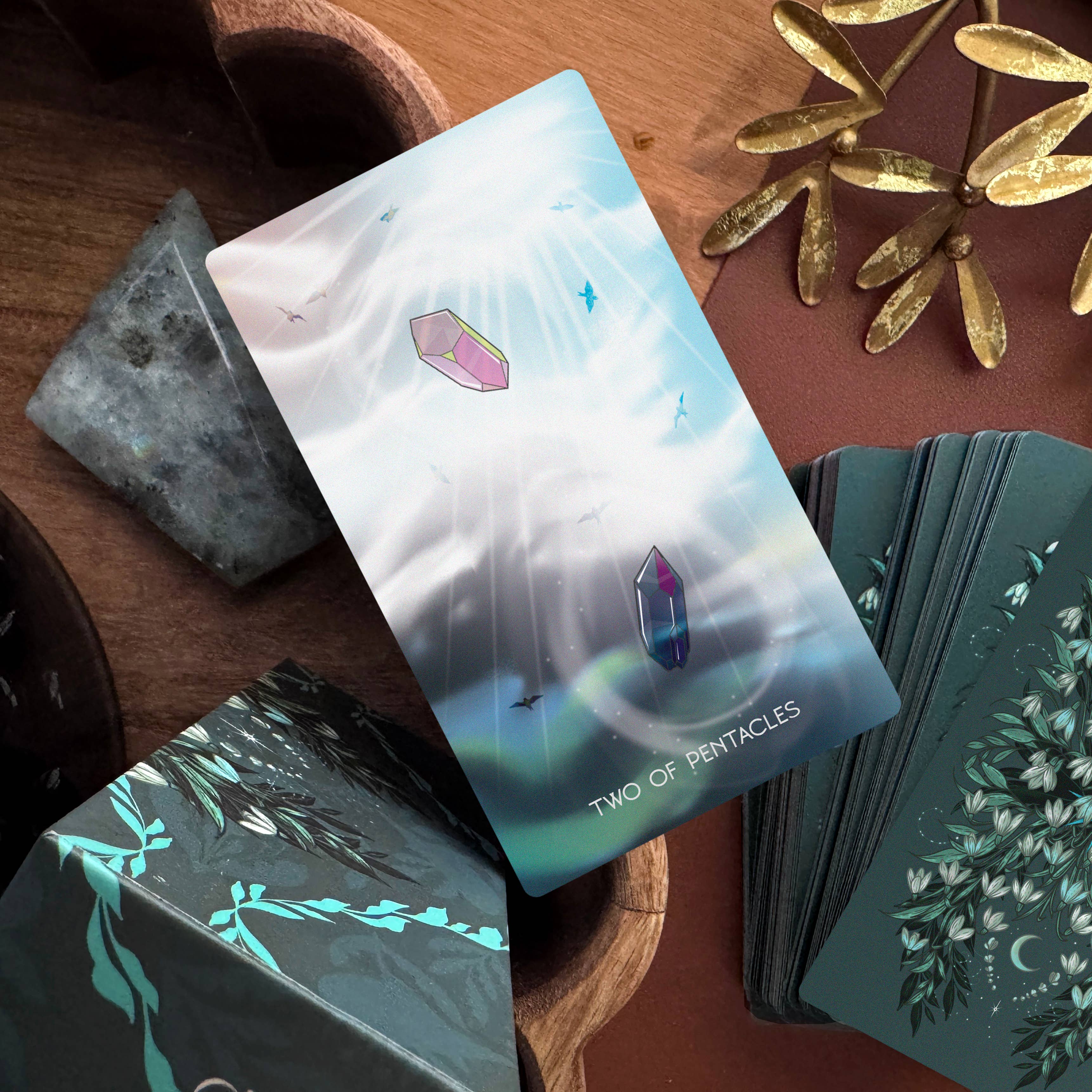 Card from a tarot or oracle deck showing two pentacles with a scenic background on a wooden surface.