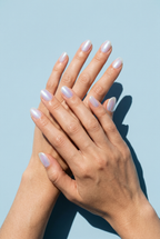 Close-up of hands with light pink nail polish against a light blue background