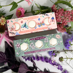 Two bath bomb boxes with floral designs on a background of flowers and greenery