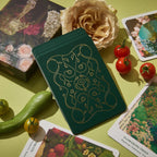 Green notebook with gold floral design on a table with cards and vegetables