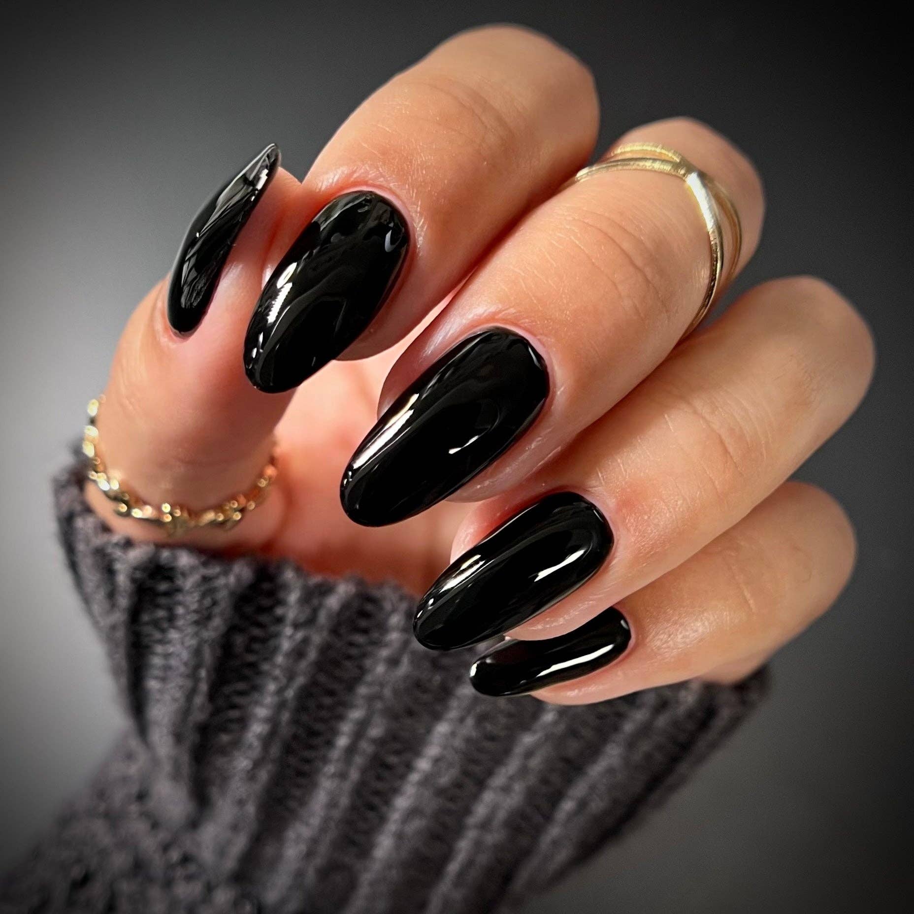Hand with black nail polish wearing gold rings on a dark background