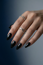 Hand with black nail polish and silver rings on a gradient background