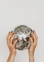 Hands holding a disco ball against a plain background