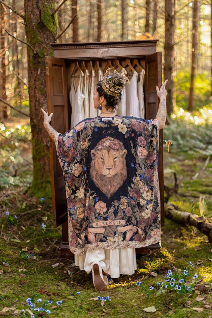 Woman in a forest wearing a robe with a lion design, standing in front of a wooden wardrobe.