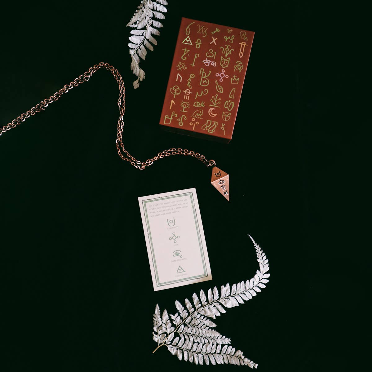 Necklace with pendant, cards, and fern leaves on a dark background