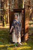 Woman in a floral dress standing next to a wooden cabinet in a forest setting