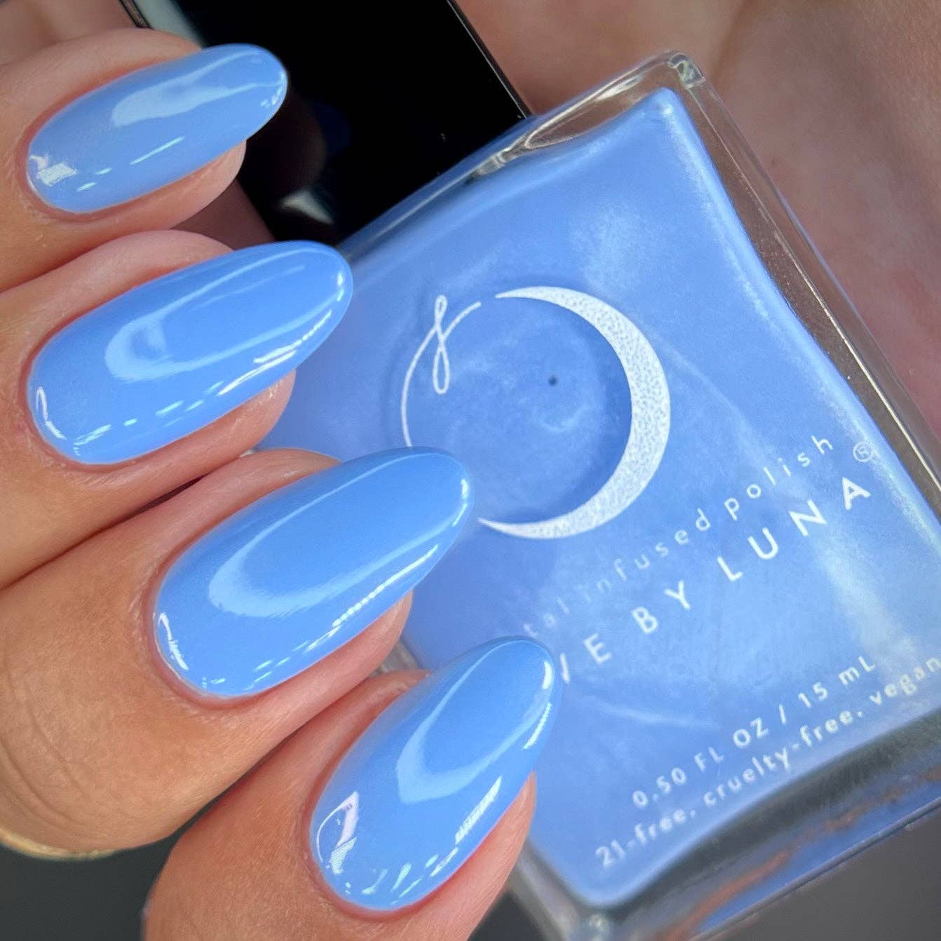 Hand with blue nail polish holding a bottle of 'Luna' nail polish.