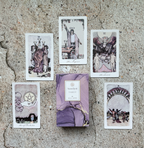 A tarot card deck box labeled 'Amethyst Tarot' sits on a textured stone surface, surrounded by five illustrated tarot cards arranged in a loose circle.