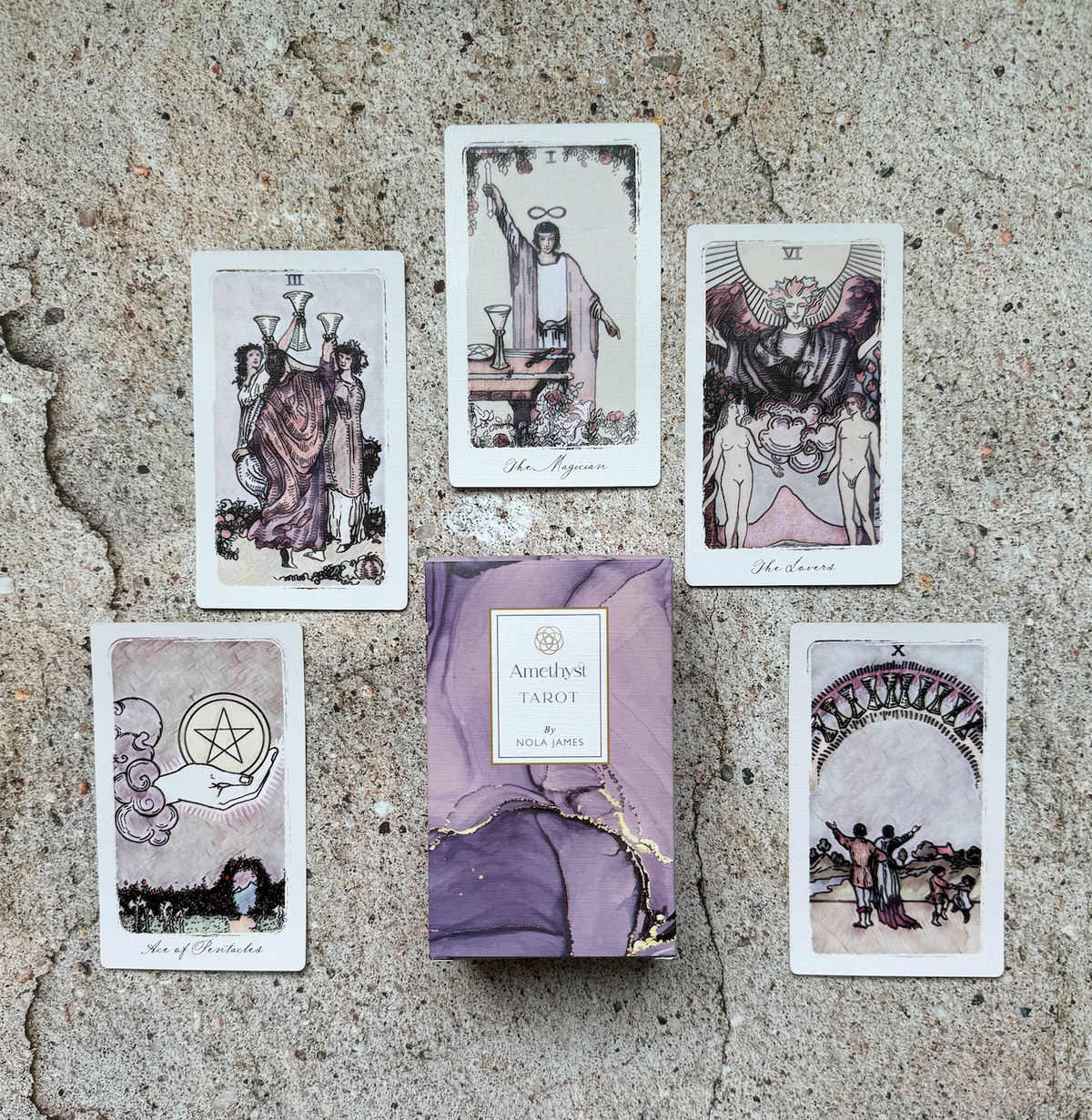 A tarot card deck box labeled 'Amethyst Tarot' sits on a textured stone surface, surrounded by five illustrated tarot cards arranged in a loose circle.