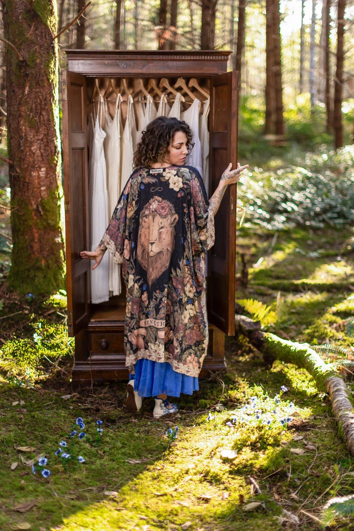 Woman in a floral dress standing next to a wooden wardrobe in a forest