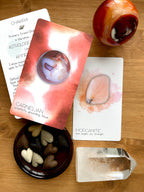 Collection of crystal-related items including cards, stones, and a crystal on a wooden surface.