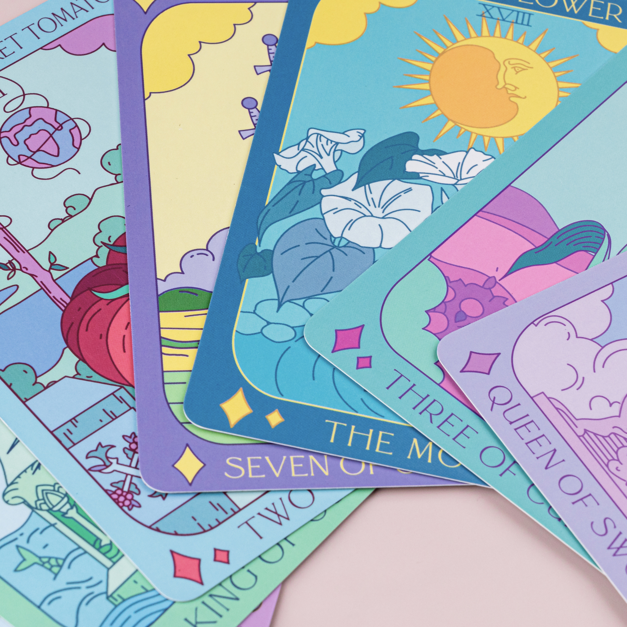 Colorful tarot cards with various symbols and designs on a light pink surface.