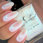 Nail polish with a hand displaying nails painted in a light pink color, and a clear bottle labeled 'Luna'.