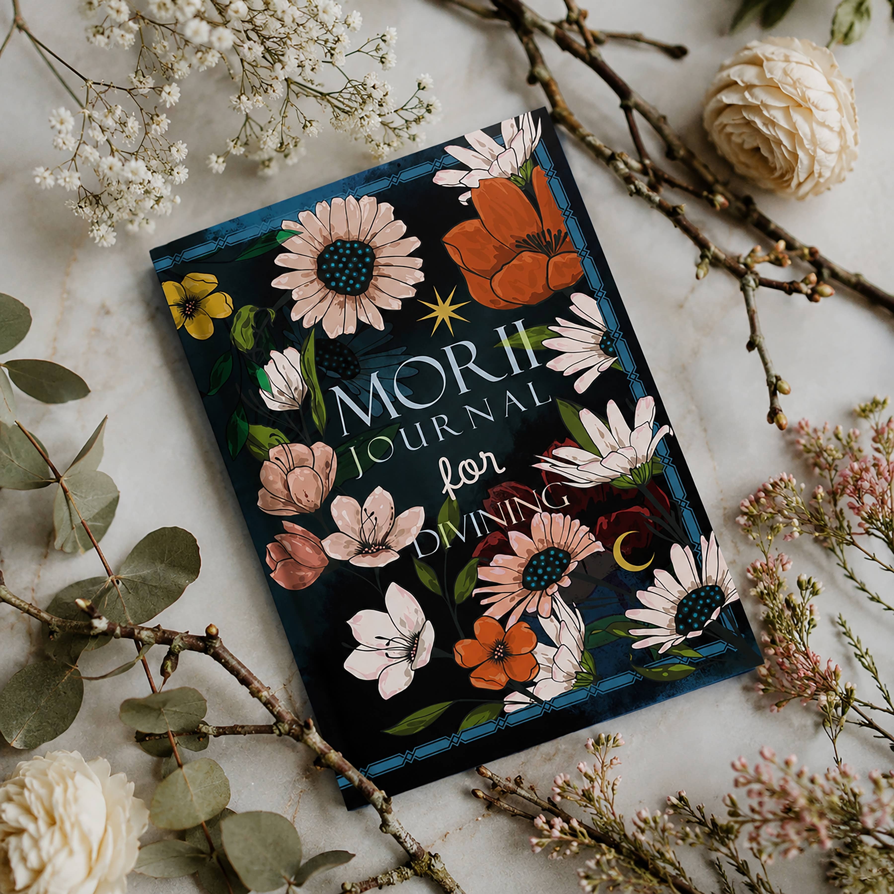 Decorative journal with floral design on a marble surface with flowers and branches.
