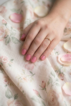 Hand with pink nail polish on a floral fabric background
