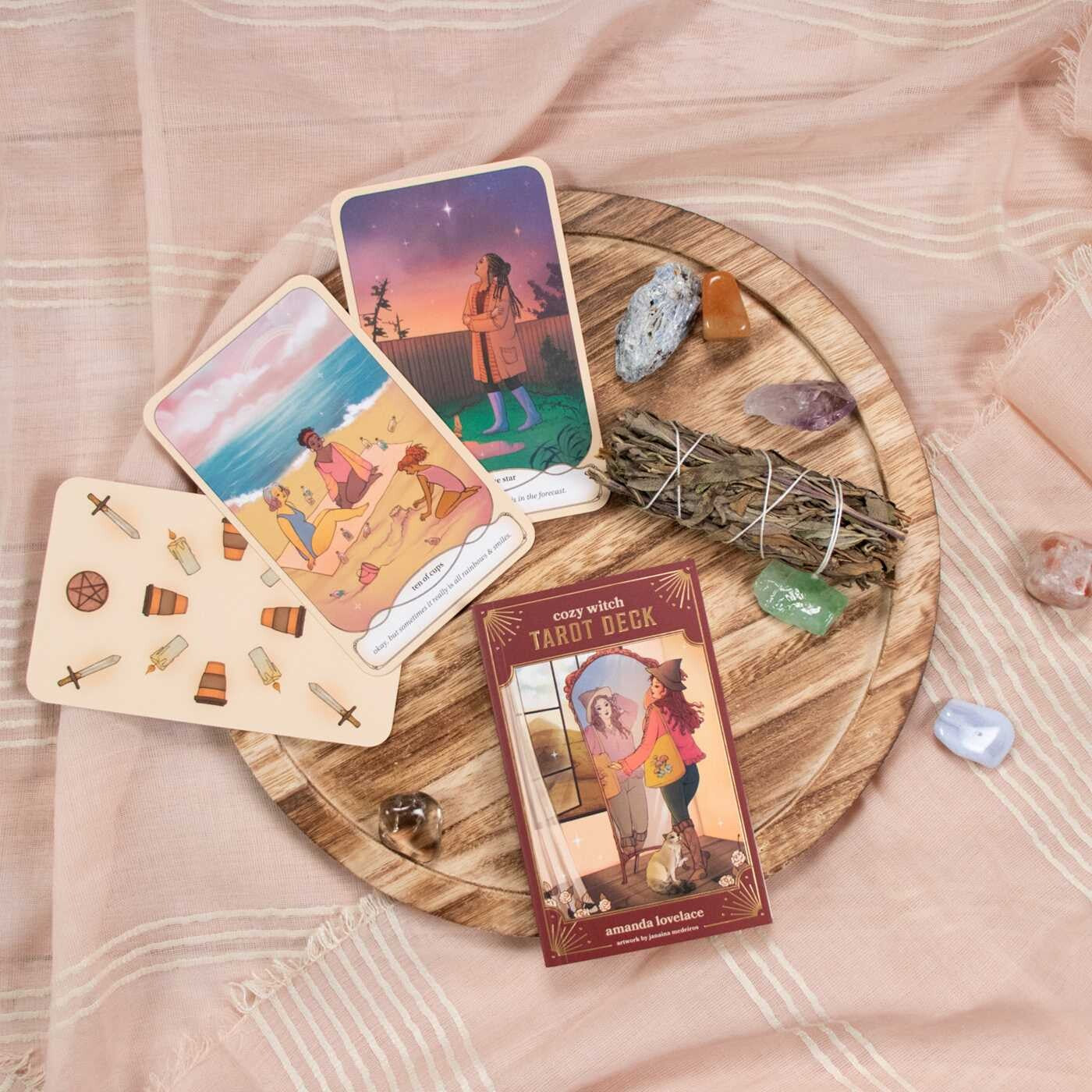 Tarot cards on a wooden board with crystals and a smudge stick on a soft pink fabric background