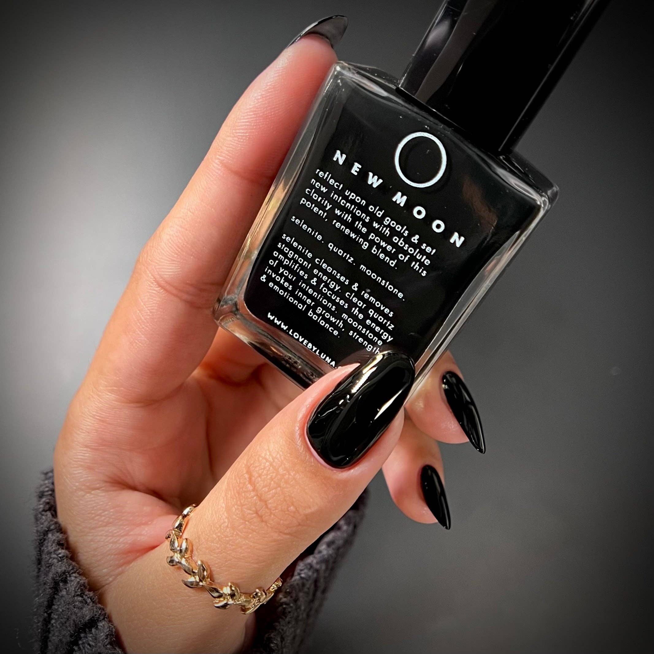Hand holding a black nail polish bottle labeled 'New Moon' against a dark background