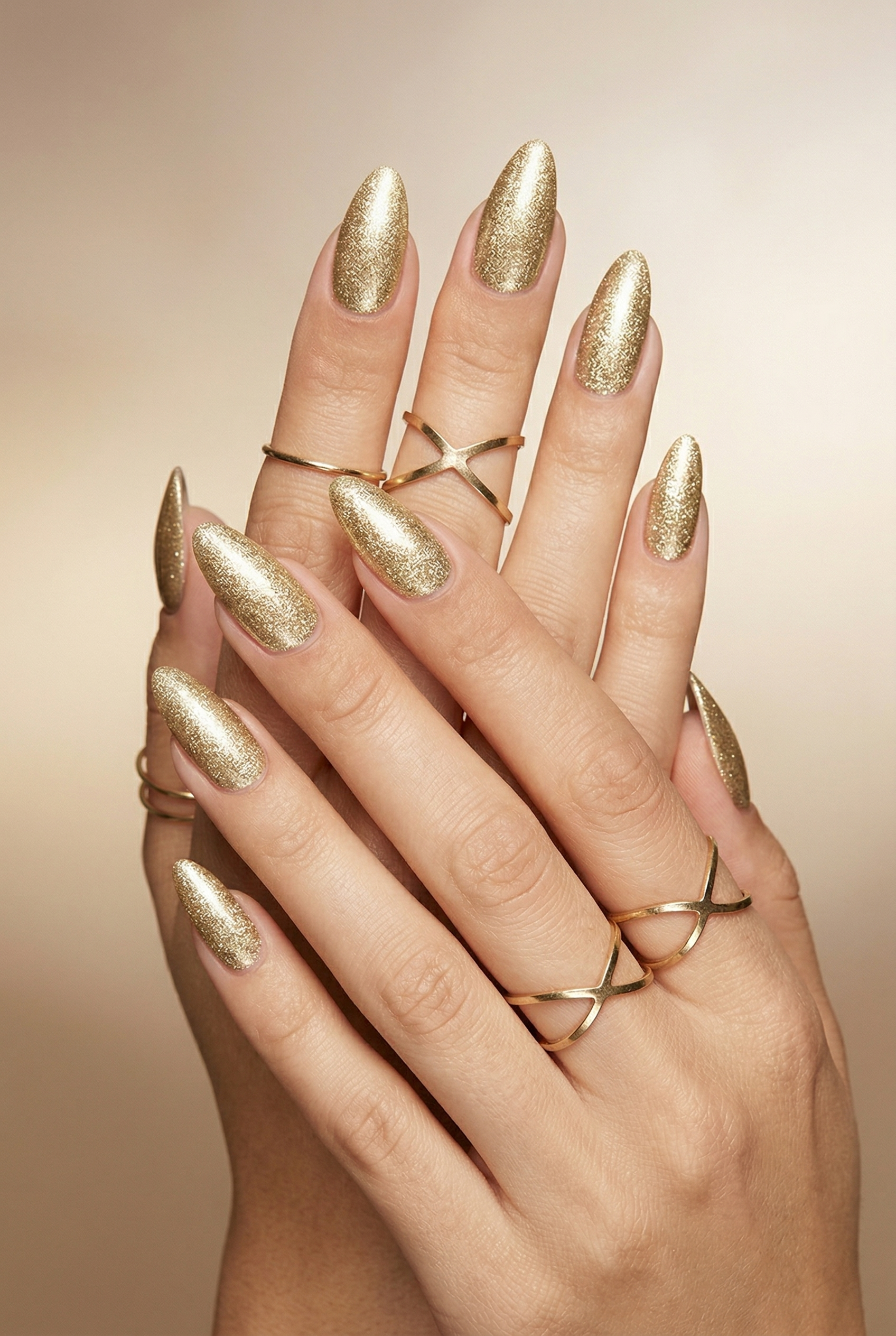 Hand with gold nail polish and rings on a beige background