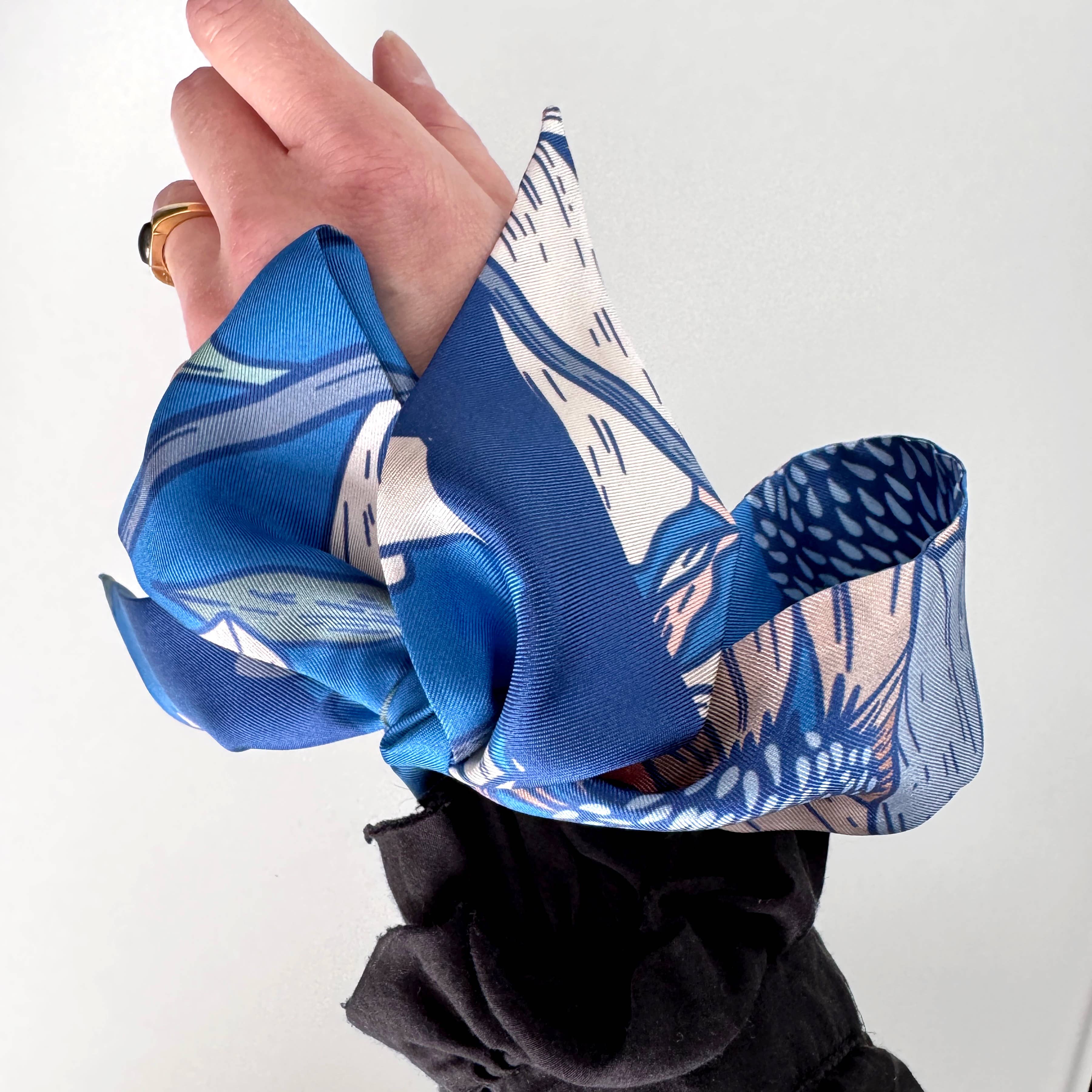 Hand holding a blue and white patterned fabric against a plain background