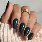 Hand with dark green nails and a gold ring on a textured surface