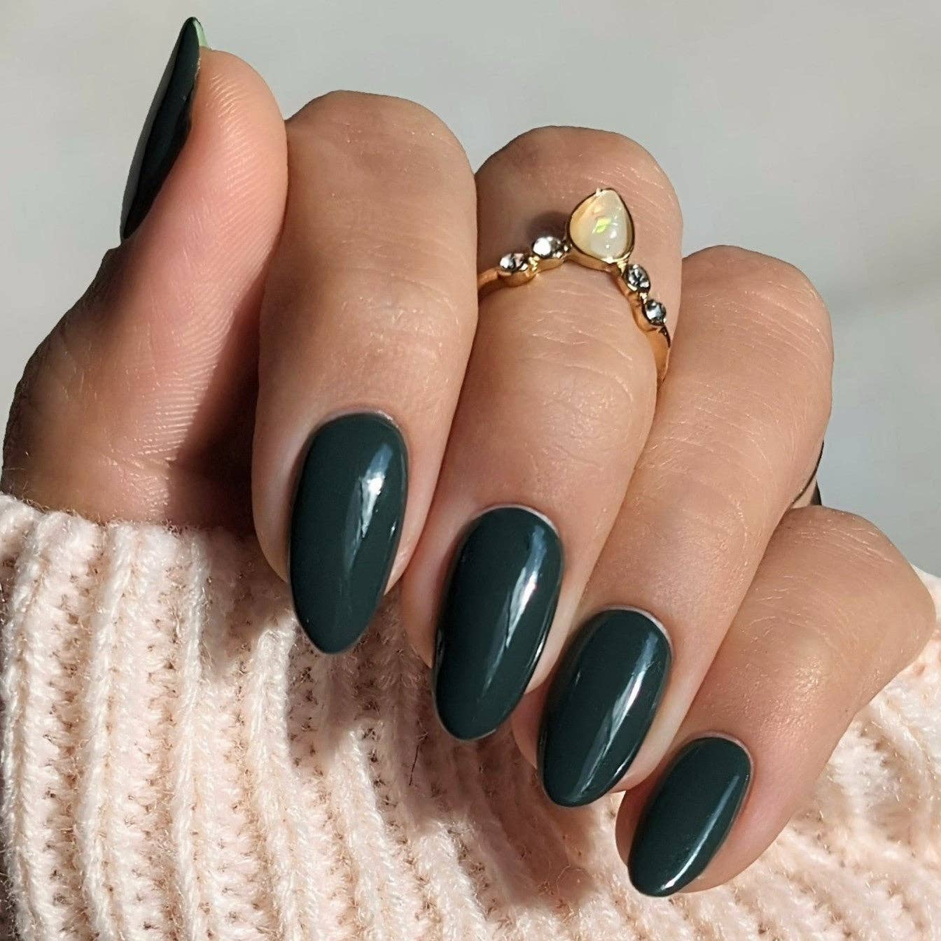 Hand with dark green nails and a gold ring on a textured surface