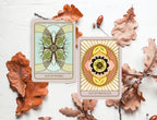 Two tarot cards, 'Ace of Wands' and 'Ace of Pentacles', surrounded by autumn leaves on a light background.