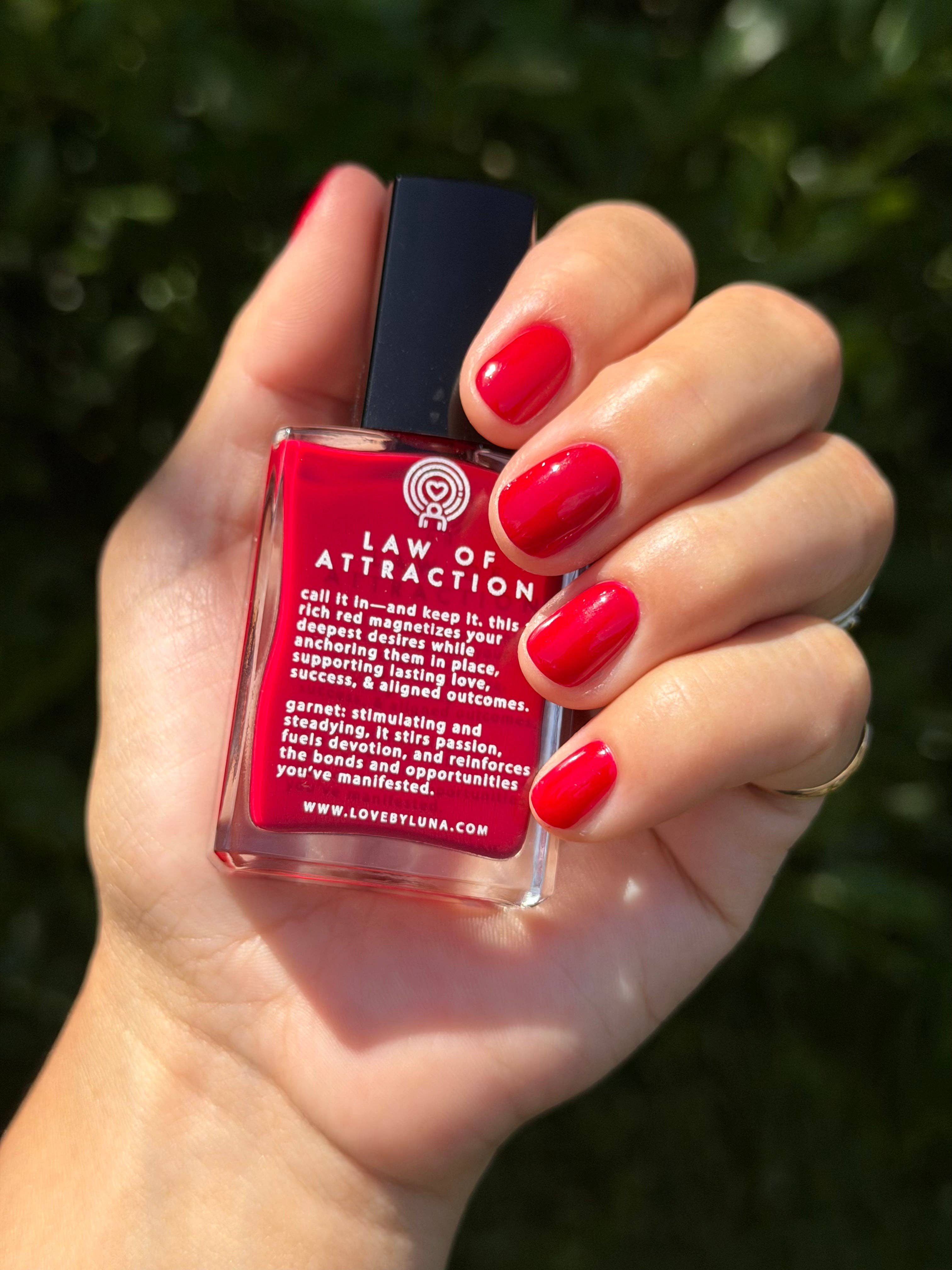 Hand holding a red bottle labeled 'Law of Attraction' against a blurred green background