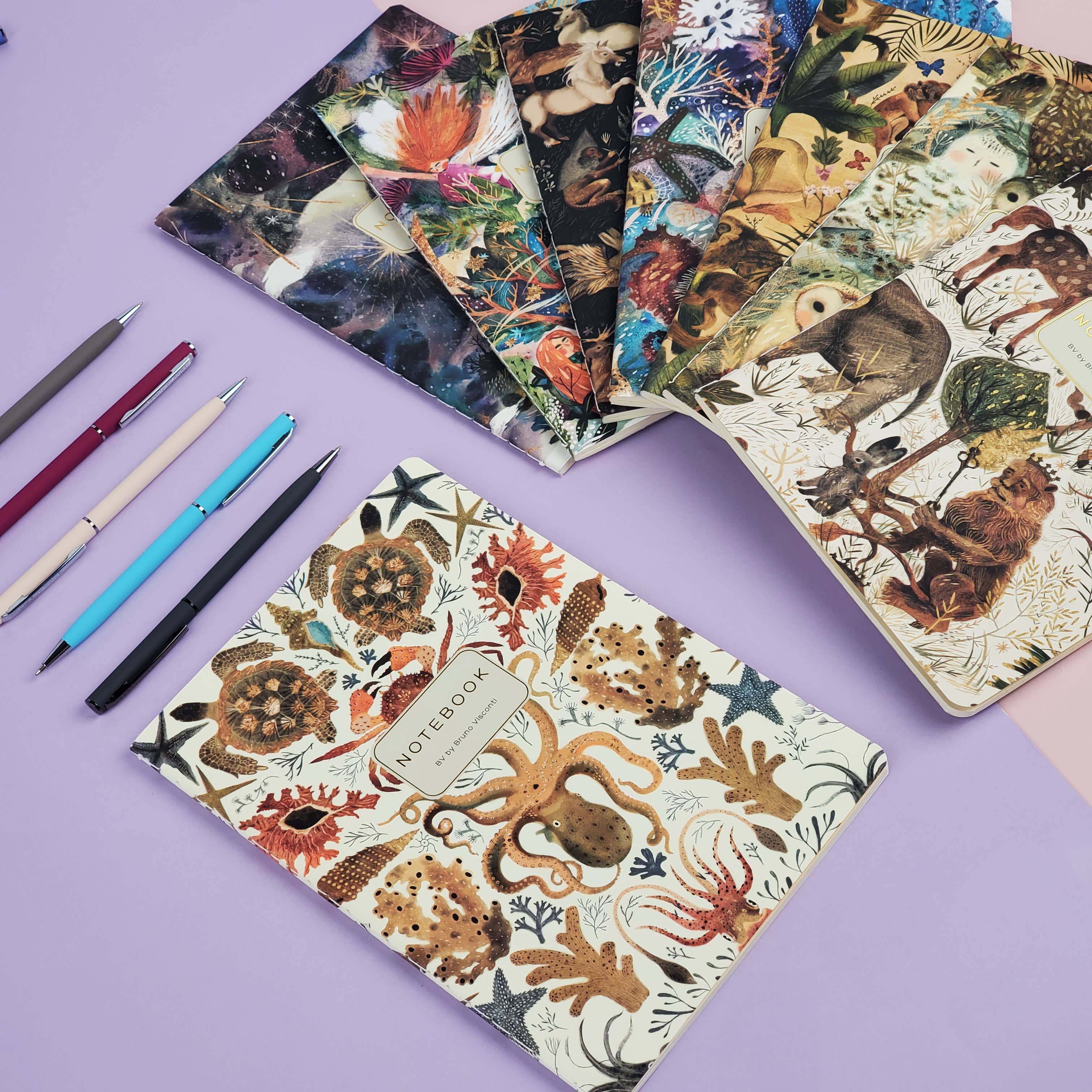 Assorted notebooks with animal-themed covers on a purple background with pens.