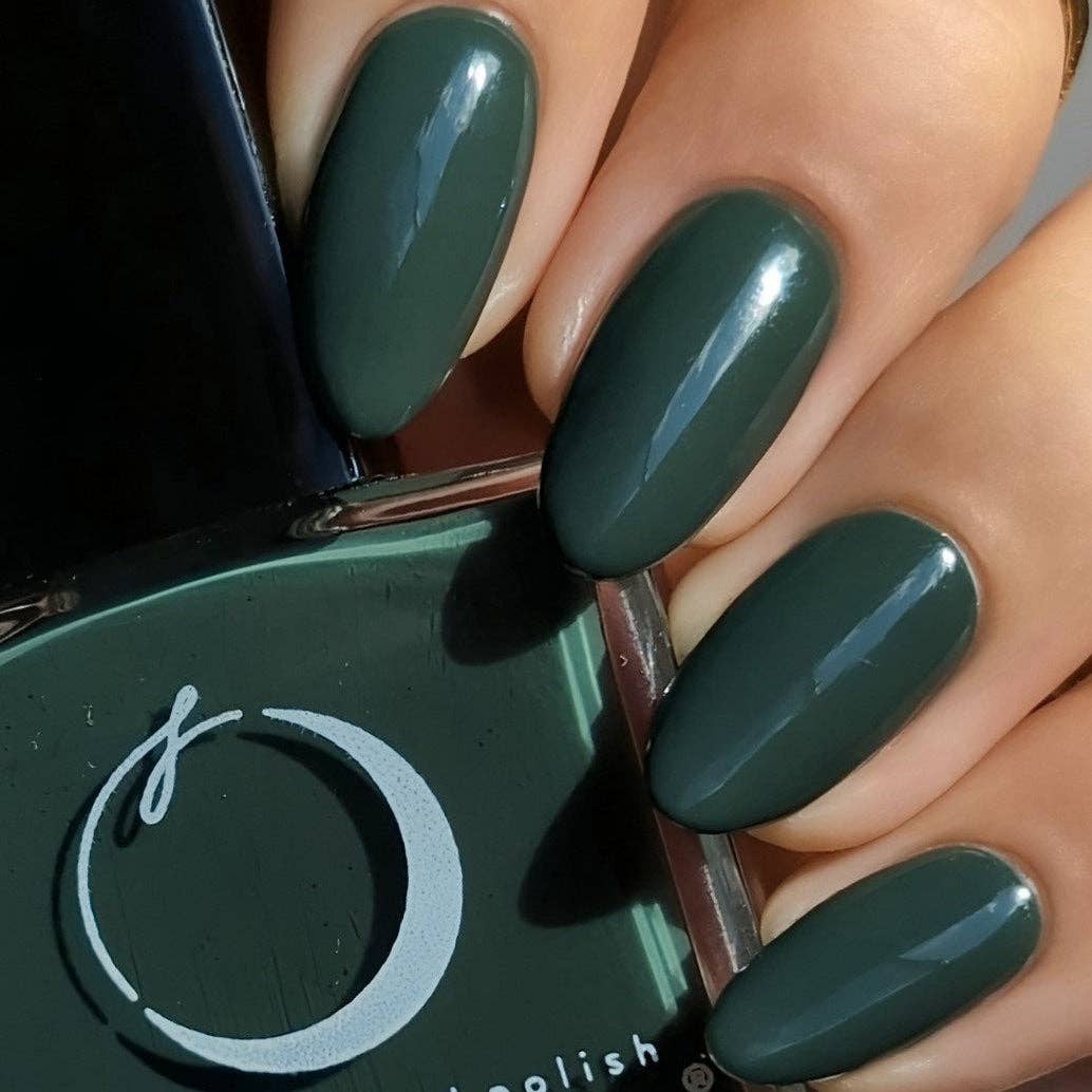 Close-up of hands with dark green nail polish holding a green nail polish bottle.