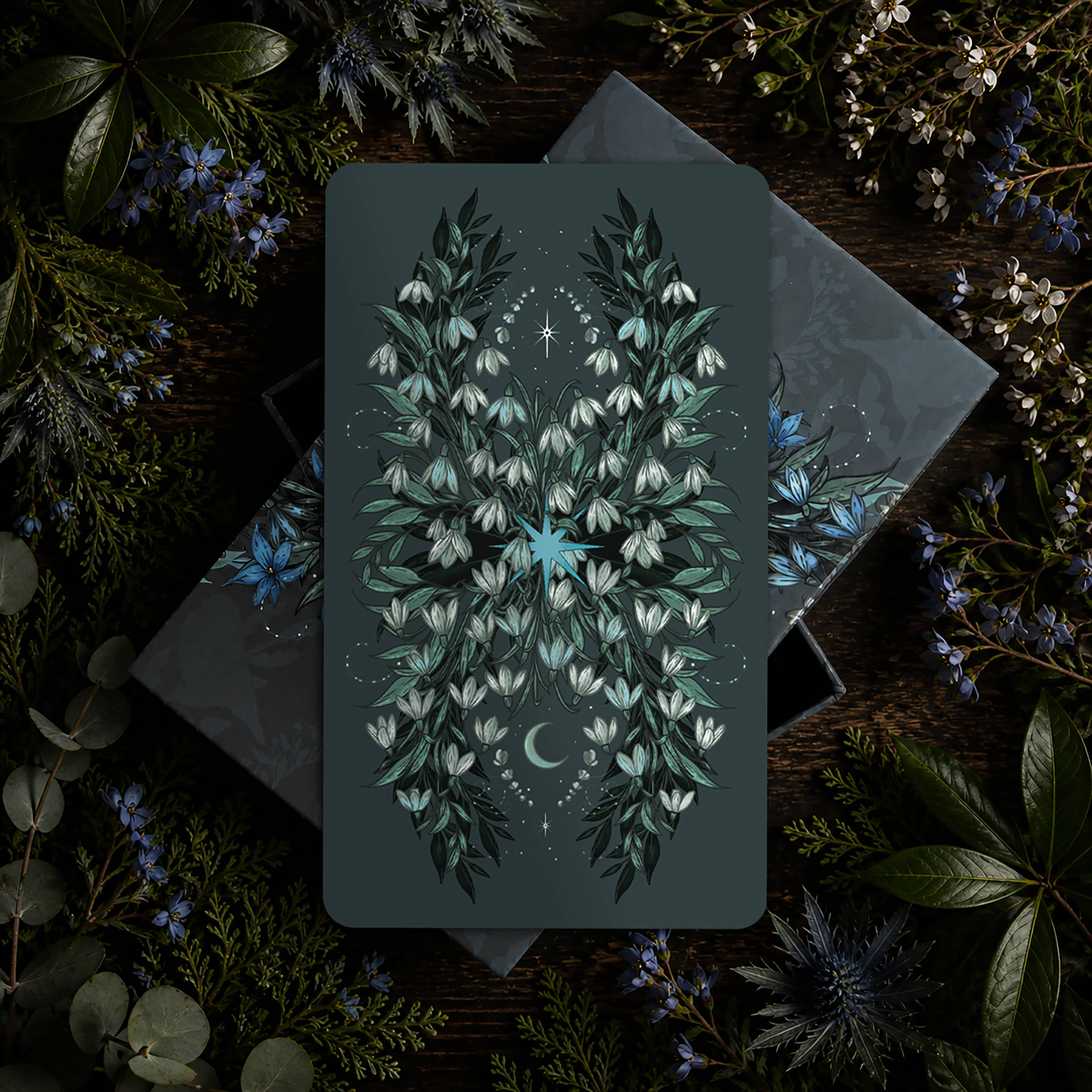 Card with floral design on a dark background surrounded by greenery
