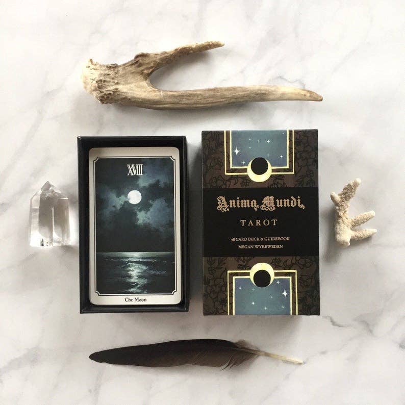 Anima Mundi Tarot set with a card featuring 'The Moon' and decorative elements on a marble surface.