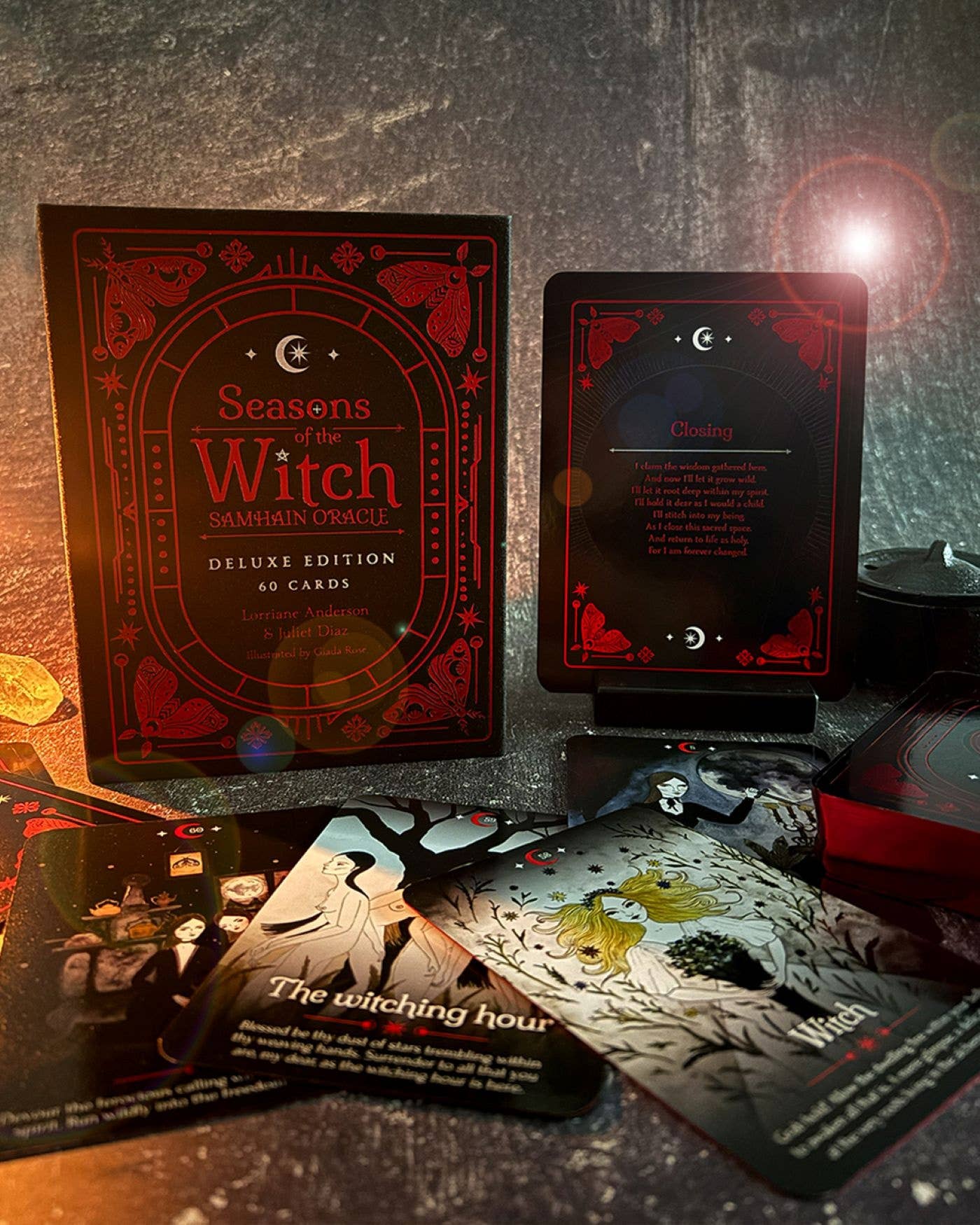 Seasons of the Witch Deluxe Edition card deck set displayed on a dark textured surface, showing the red and black illustrated box, a single card face, and several fanned-out cards including 'The witching hour'.