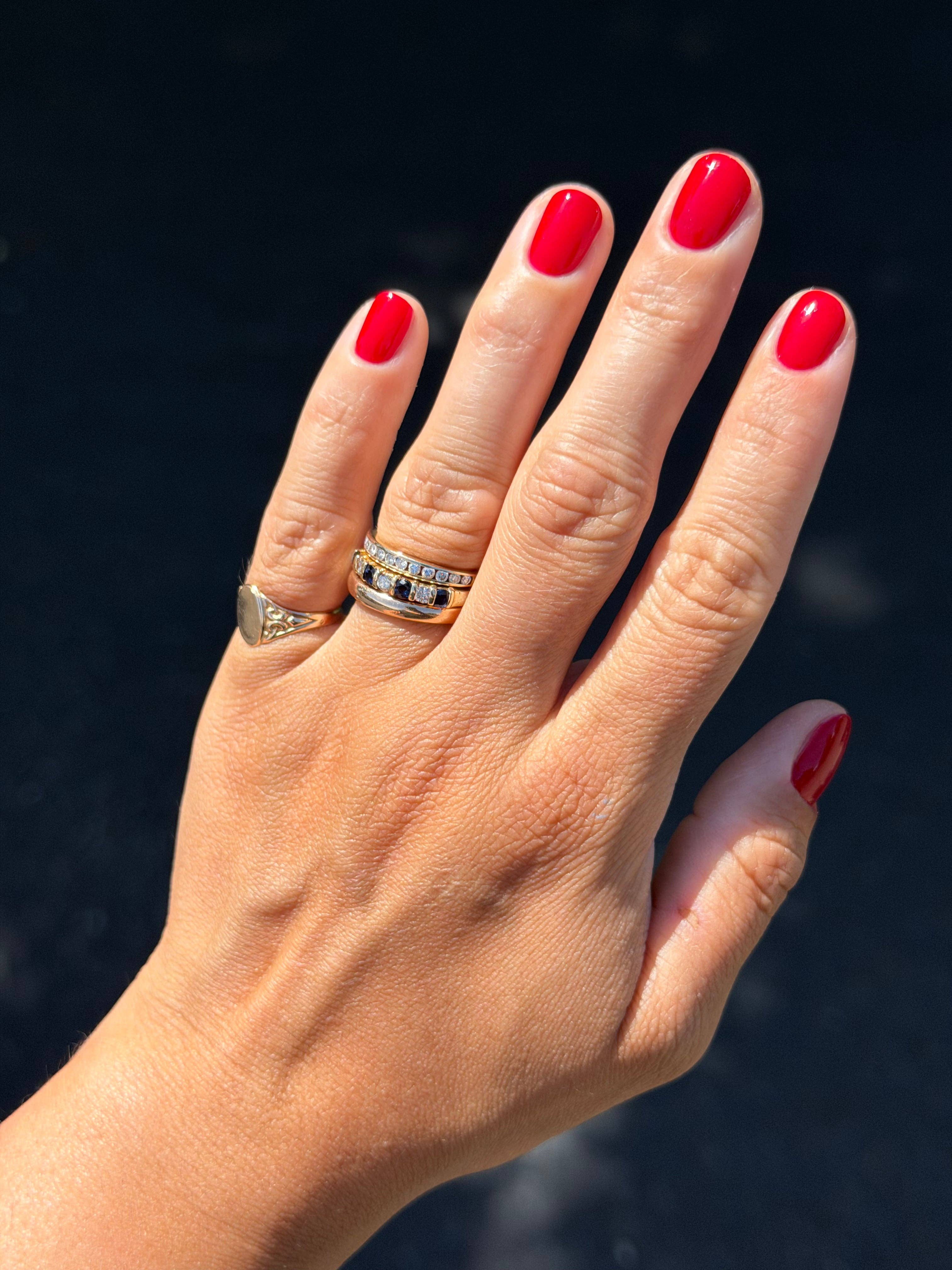 Hand with red nail polish wearing two rings against a dark background