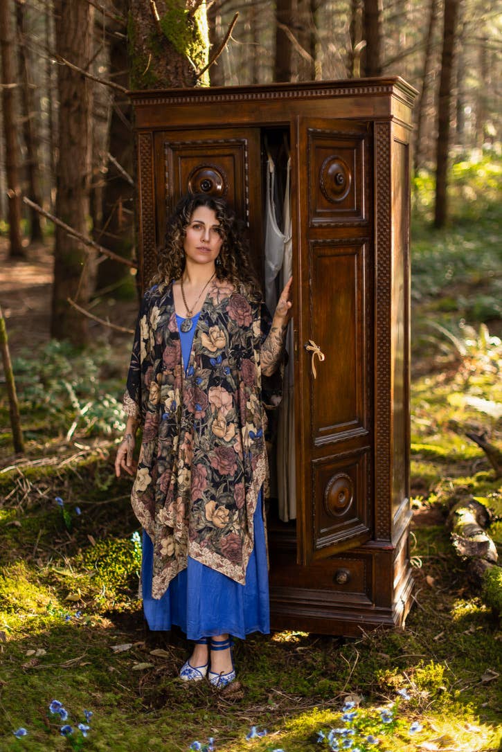 Woman standing in a forest with an open wooden wardrobe