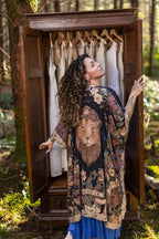 Woman in a patterned kimono standing in front of an open wooden wardrobe in a forest setting.