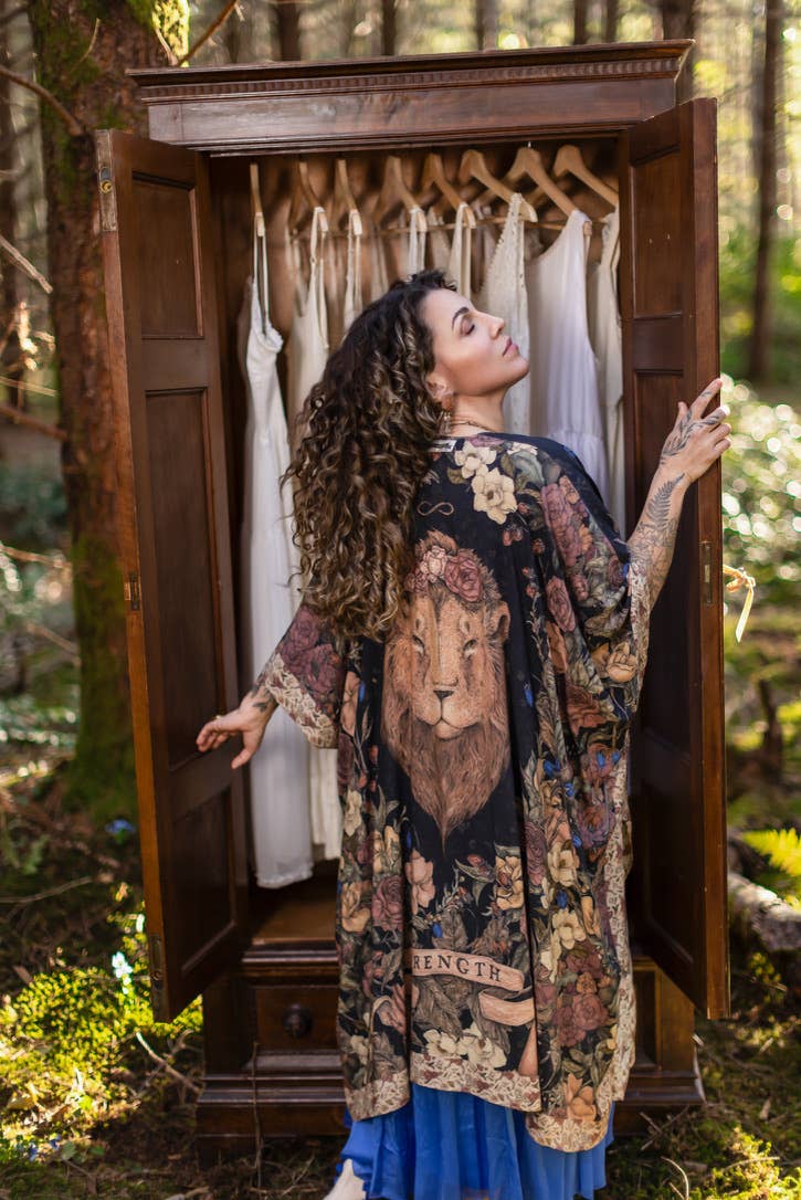 Woman in a patterned kimono standing in front of an open wooden wardrobe in a forest setting.