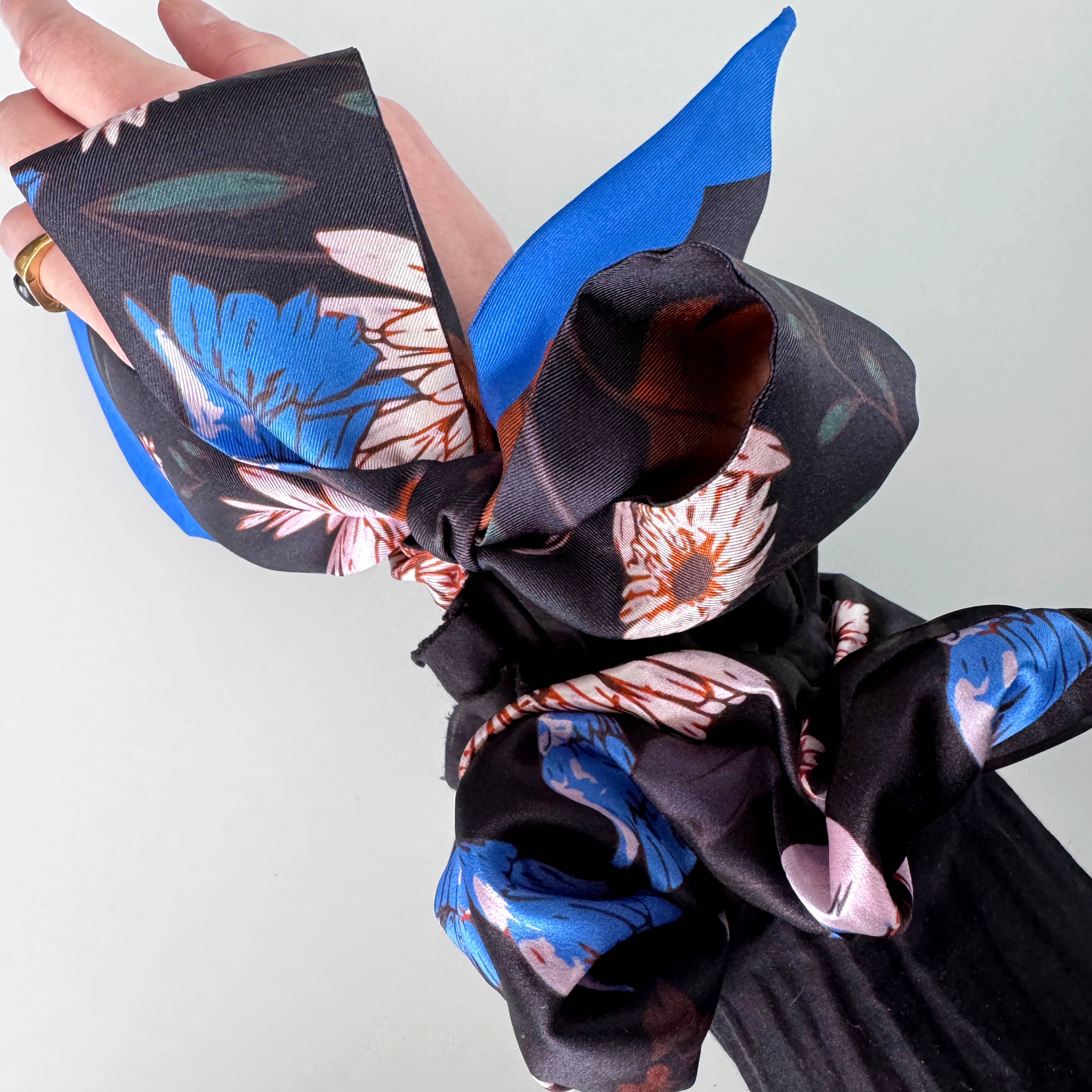 Floral-patterned fabric with black border held by a hand against a light gray background