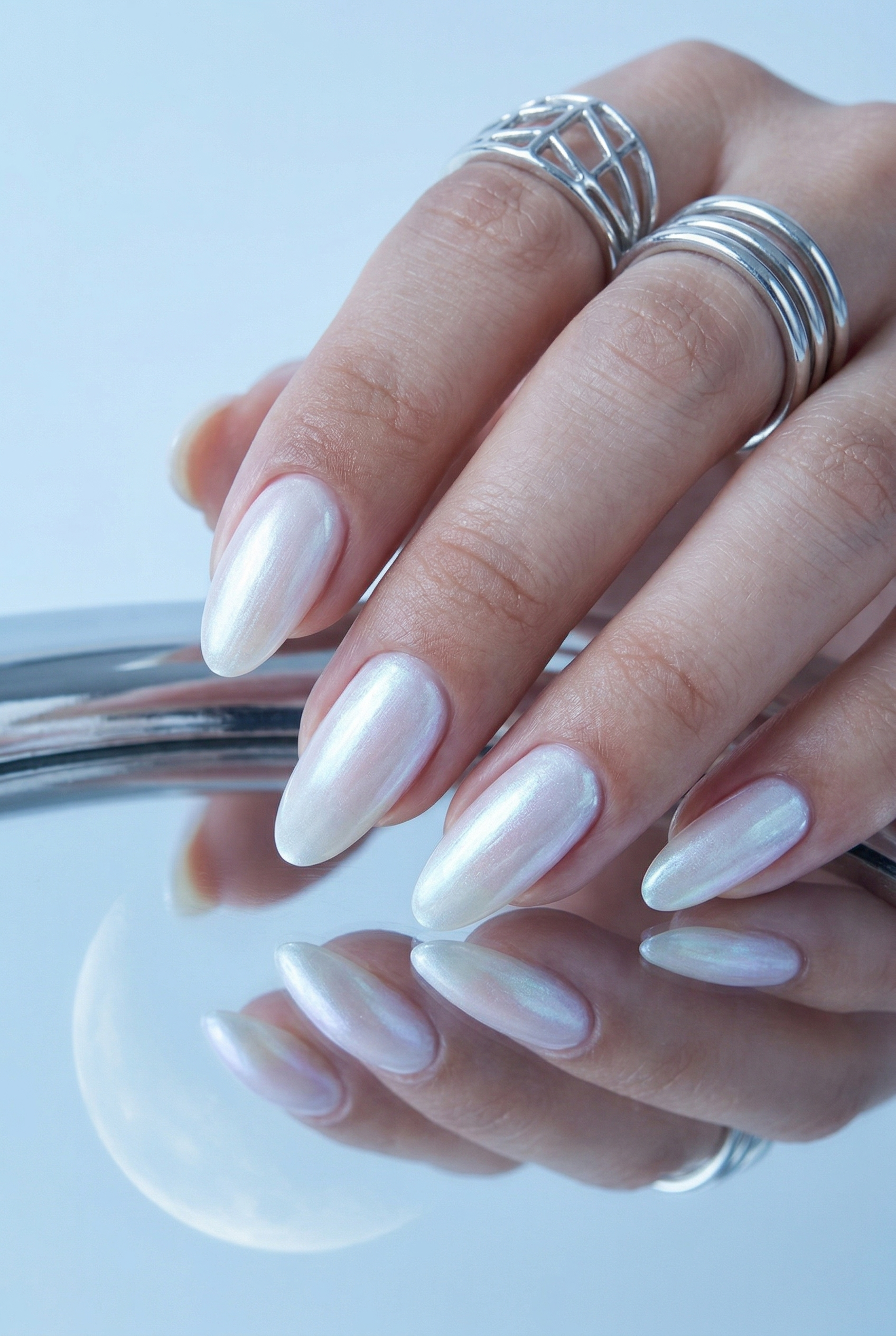 Close-up of a hand with white nail polish and silver rings on a light blue background