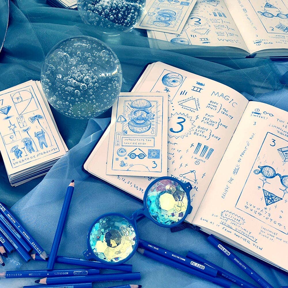 Blue stationery items including pens, pencils, and a notebook with blue designs on a blue surface.